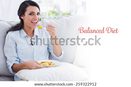 The word balanced diet against happy woman sitting on the sofa eating fruit salad