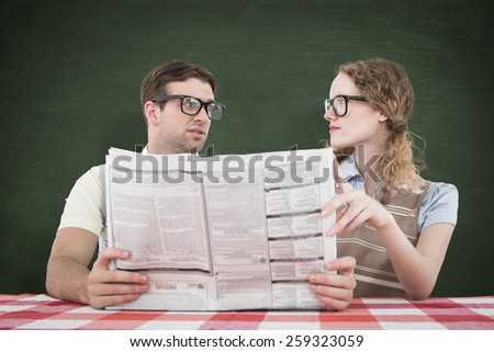 Geeky hipster couple reading newspaper against green chalkboard