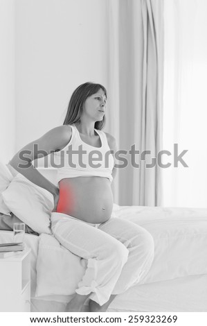 Charming pregnant female having a back pain while sitting on a bed in her apartment