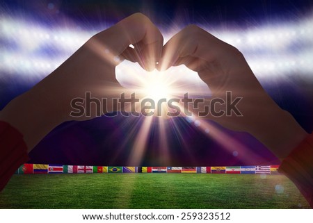 Woman making heart shape with hands against football pitch with world cup flags