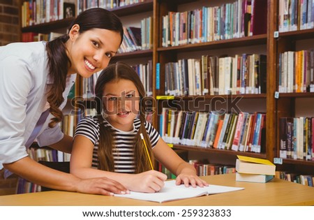 Portrait of teacher assisting little girl with homework in the library