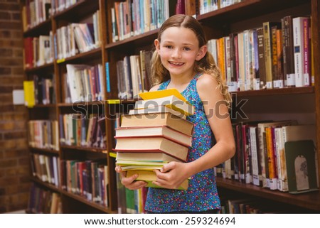 Portrait of cute little girl carrying books in the library