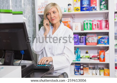Blonde pharmacist using computer while phoning in the pharmacy