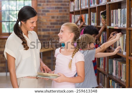 Cute pupils and teacher looking for books in library at the elementary school