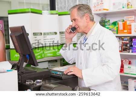 Senior pharmacist phoning while using computer in the pharmacy