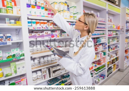Junior pharmacist taking medicine from shelf in the pharmacy