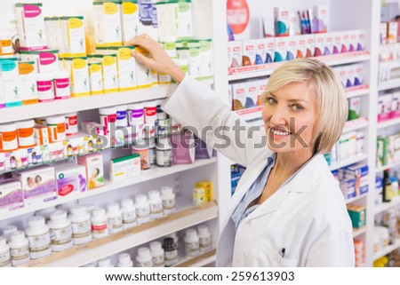 Smiling pharmacist taking box from shelf in the pharmacy