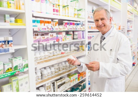 Smiling senior pharmacist holding medicine and prescription in the pharmacy