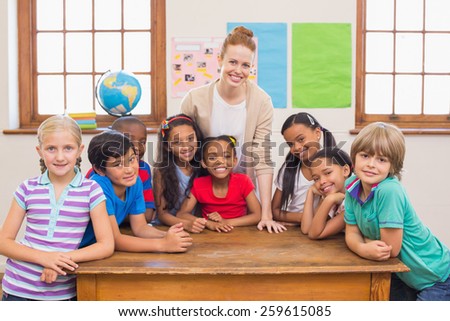 Cute pupils and teacher smiling at camera in classroom at the elementary school