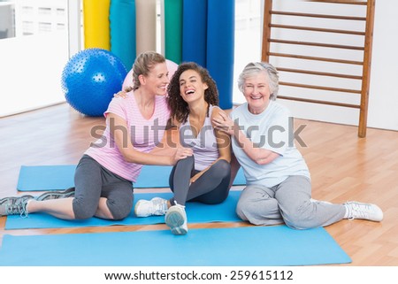 Playful female friends sitting together on exercise mat in gym