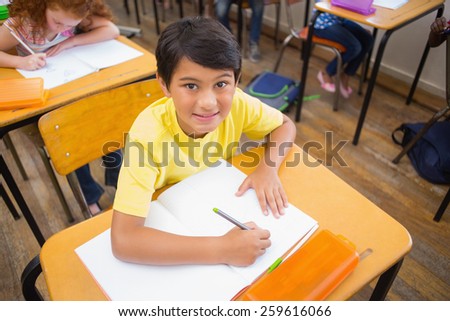 Cute pupils drawing at their desks one smiling at camera at the elementary school