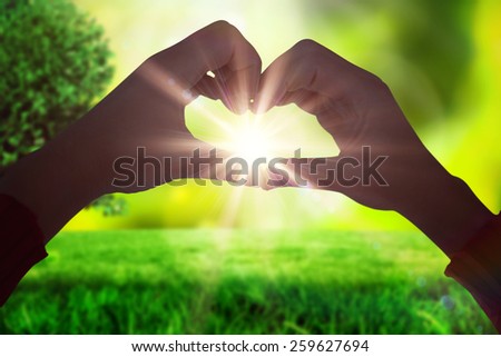 Woman making heart shape with hands against field against glowing lights