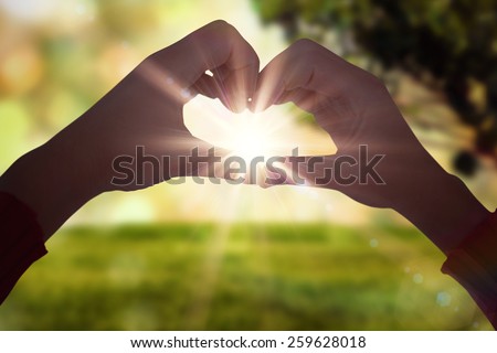 Woman making heart shape with hands against field against glowing lights