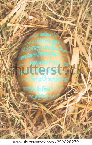 Happy easter in different languages against gold egg in the straw