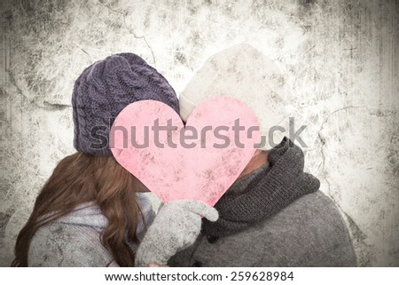 Couple in warm clothing holding heart against grey background