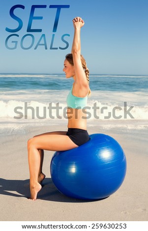 Fit woman sitting on exercise ball at the beach stretching arms against set goals