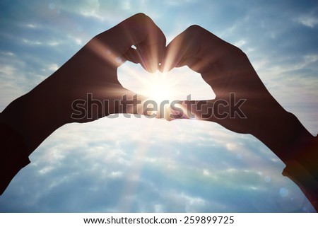 Woman making heart shape with hands against clouds reflected on water