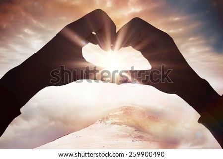 Woman making heart shape with hands against misty landscape