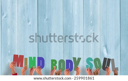 Hands holding up mind body soul against wooden planks