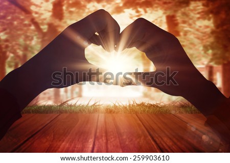Woman making heart shape with hands against wooden planks overlooking tree lined path