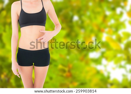 Closeup mid section of a fit woman with hand on stomach against detail shot of bright green leaves