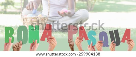 Hands holding up bona pasqua against little girl sitting on grass counting easter eggs smiling at camera
