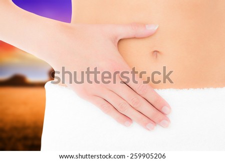 Mid section of a fit woman with hand on stomach against countryside scene