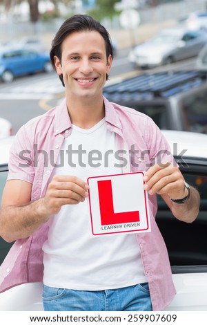 Learner driver smiling and holding l plate in front of his car