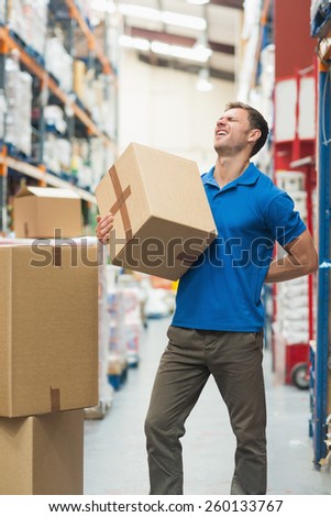 Side view of worker with backache while lifting box in the warehouse