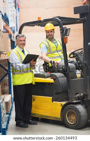 Driver operating forklift machine next to his manager in warehouse