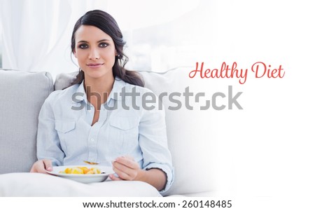 The word healthy diet against pretty woman sitting on the couch eating fruit salad
