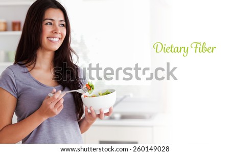 The word dietary fiber against attractive woman enjoying a bowl of salad while standing