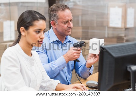 Manager scanning box while his colleague typing on laptop in a large warehouse