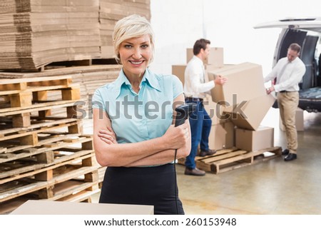 Warehouse manager holding scanner with arms crossed in a large warehouse