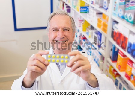 Senior pharmacist holding up blister packs at hospital pharmacy