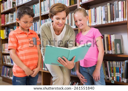 Teacher reading book with pupils at library at elementary school