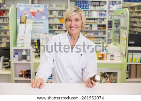Smiling pharmacist holding medicine jar at pharmacy