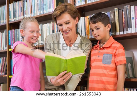 Teacher reading book with pupils at library at elementary school