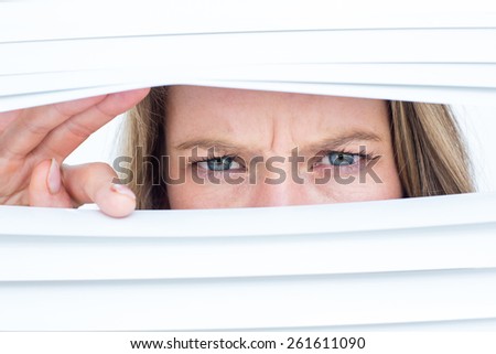 Woman peering through roller blind on white background
