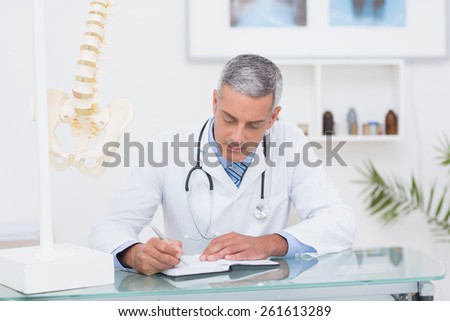 Doctor writing on diary at his desk in medical office