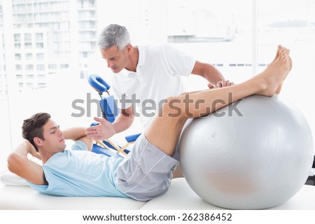 Therapist helping his patient with exercise ball in medical office