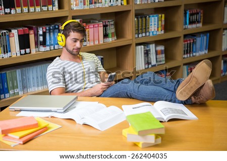 Student listening music in the library with smartphone at the university