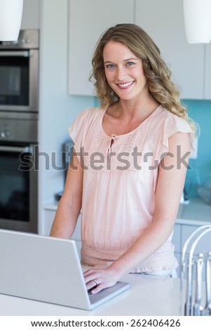 Pretty blonde using her laptop at home in the kitchen