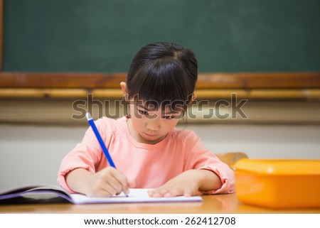 Cute pupil writing at desk in classroom at the elementary school