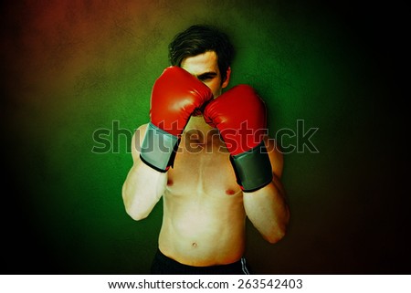 Muscly man wearing red boxing gloves in guard position against dark background