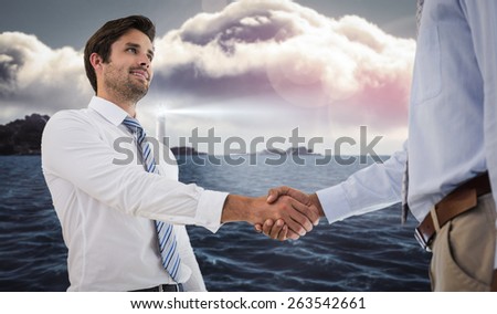 Young businessmen shaking hands in office against calm sea with lighthouse