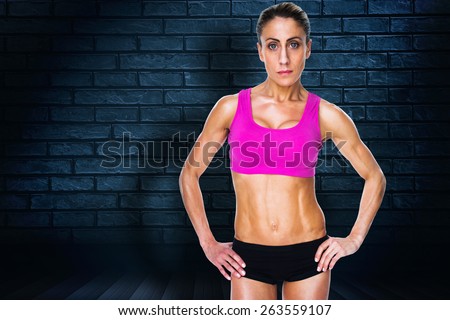 Female bodybuilder posing with hands on hips looking at camera against black background