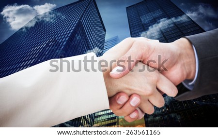 Close up on partners shaking hands against low angle view of skyscrapers