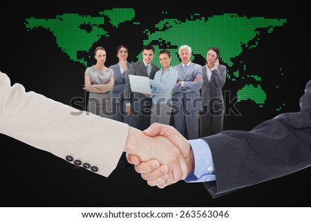 Smiling business people shaking hands while looking at the camera against blue world map