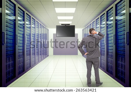 Young businessman standing back to camera scratching his head against server room with towers